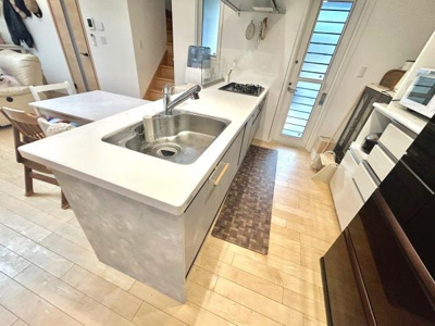 キッチン全体がホワイトで統一されており清潔感があります。大きなシンクと広めの作業スペースが特徴的です。背面収納も豊富で整理整頓がしやすいです。床も明るい色合いで空間が広く感じられます。