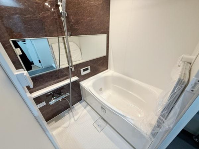 落ち着いた色合いの壁面パネルが洗練された印象を与えるバスルームです。広々とした浴槽が設置されておりリラックスできる空間となっています。大きめのミラーが採用されていて使い勝手にも配慮されています。