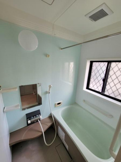 大きな窓があり明るい雰囲気のバスルームです。手すりやベンチ付きで使いやすさを感じます。浴槽も広めの設計で快適に利用できます。清潔感のある配色が印象的です。