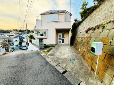 前面道路から敷地までのアプローチが印象的な現地写真です。開放感のある高台立地で空の広がりと周囲の見通しも良好です。駐車スペースも備わっており生活動線に配慮された住まいです。