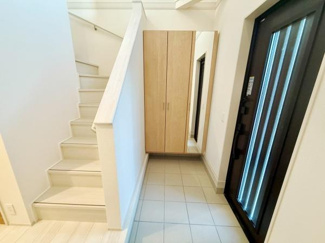 明るい玄関スペースが広がっています。大型の収納があり靴や小物の整理に役立ちます。白を基調とした内装が清潔感を演出しています。階段への動線もスムーズで使いやすい設計です。