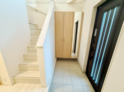 明るい玄関スペースが広がっています。大型の収納があり靴や小物の整理に役立ちます。白を基調とした内装が清潔感を演出しています。階段への動線もスムーズで使いやすい設計です。