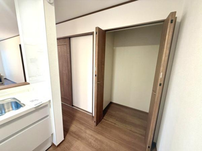 シンプルで広々としたクローゼットが備わっています。木目調の扉が空間に落ち着いた印象を与えます。キッチンのすぐそばにあり日常の使い勝手を考えた設計です。収納スペースが確保され日用品の整理にも便利です。