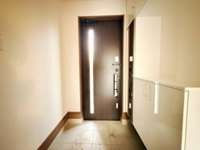 明るい玄関スペースが広がっています。清潔感のある床と白を基調とした収納が印象的です。シンプルなデザインの扉が空間に調和しています。収納力のあるシューズボックスも備わっています。使い勝手の良い玄関です。