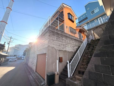 現地は高台に位置し道路からのアクセスが特徴的です。前面道路は幅が広めで車の通行もスムーズです。建物の外観は鮮やかなカラーが目を引きます。階段やフェンスがしっかりと設置されています。