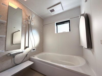 大きな窓があり明るい自然光が差し込むバスルームです。白を基調とした清潔感あふれるデザインです。鏡や収納棚が便利に配置されています。浴槽とシャワーエリアがゆとりのある設計です。換気設備が整っています。