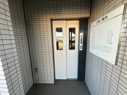エントランスには使いやすいエレベーターが設置されています。シンプルなホワイトドアが空間と調和しています。フロア案内板も備えられており移動がスムーズに行えます。清潔感のあるタイル貼りの壁面が特徴的です。