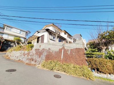 現地の様子がしっかりと分かる前面道路を含んだ写真です。敷地まわりの石垣や植栽の手入れも確認できます。周囲の住宅との距離感もしっかりと映されています。日差しがしっかり入る明るい雰囲気です。