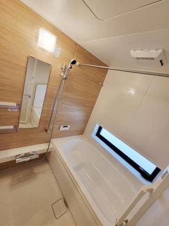 やわらかな木目調パネルがアクセントの浴室です。窓付きで換気にも配慮されています。シンプルなデザインで日常使いに便利です。鏡や手すりも備わっており快適な仕様です。明るい照明が室内をしっかり照らします。