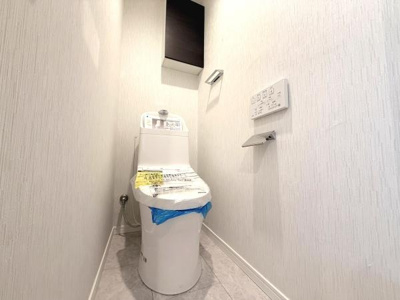 白を基調としたトイレで清潔感のある内装です。壁に操作パネルが設置されており利便性が感じられます。収納スペースも備わっていてすっきりとした空間です。床も手入れしやすい素材で日々の管理がしやすいです。