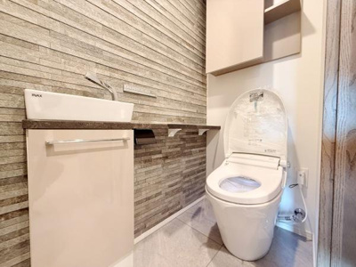 スタイリッシュな壁面デザインが印象的なトイレです。手洗いカウンターと収納棚が備わっており機能的な空間となっています。清潔感のある内装で日々のお手入れもしやすい仕様です。ゆとりのあるスペースが特徴です。