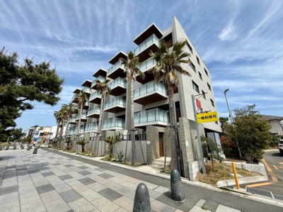 リゾート感のある外観が目を引くマンションです。バルコニーが特徴的で開放的なデザインとなっています。ヤシの木が並ぶエントランス周辺が印象的です。通路や植栽も整えられ清潔感があります。