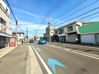 青空が広がる前面道路は見通しが良く周囲には店舗も並んでいます。歩道も整備されており公共の交通手段も利用しやすい環境です。電線が整然と配置され街並みが整っています。現地の雰囲気がしっかり伝わる写真です。