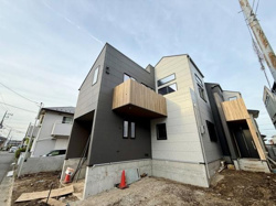 現地の様子が一目で分かる前面道路を含む写真です。建物の工事状況や周辺の住宅環境が映っています。日差しの下で敷地全体が明るく見渡せます。
