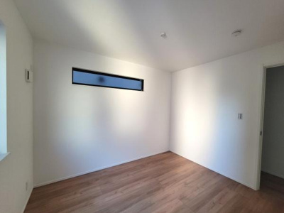 シンプルなデザインの洋室で落ち着いた雰囲気が広がります。床の木目調が温かみを感じさせます。横長の窓が室内に自然光を取り入れ明るさを保っています。壁や天井も白色でまとめられており清潔感があります。