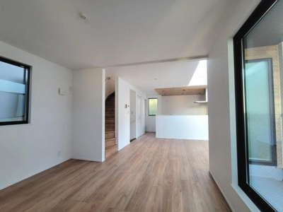 リビングは大きな窓から光が差し込み明るさを感じられます。木目調の床が空間に温かみを与えています。天井まで続く壁が開放感を演出しています。シンプルな内装が好印象です。キッチンとも程よくつながっています。