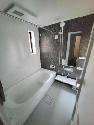 浴槽と洗い場がゆったりとしたバス空間です。窓があり換気や採光にも配慮されています。ブラック調のアクセントパネルが印象的です。シャワーヘッドや収納スペースも設置されています。床は滑りにくい素材です。