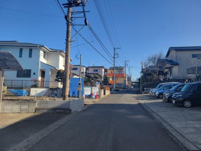 前面道路は舗装されており車両の通行も安心です。周辺には住宅や駐車場が整然と並んでいます。道路沿いには電柱もありインフラ設備も確保されています。日当たりの良いエリアとなっています。