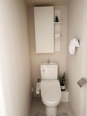 収納スペースが設けられたトイレとなっています。コンパクトながらも清潔感のある内装です。観葉植物がアクセントとなり落ち着いた雰囲気を演出しています。手洗い器付きのタンクで便利に使えます。