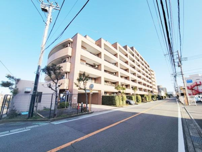 明るい青空の下しっかりした構造の建物外観が印象的です。通り沿いの整備された街路樹やきれいに管理された植栽が見受けられます。広い道路に面しているため開放感があります。