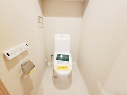 棚付きのトイレで収納が確保されています。落ち着いた色合いの内装が特徴です。温水洗浄便座のリモコンも設置されています。清潔感のある空間となっています。
