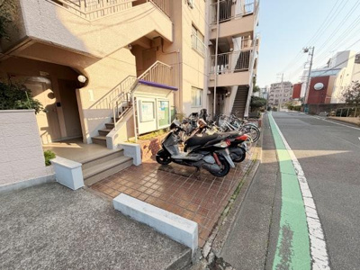 建物エントランス横にはバイクや自転車の駐輪スペースがあります。歩道に面した立地で移動にも便利です。入口部分は段差が低めで出入りしやすくなっています。