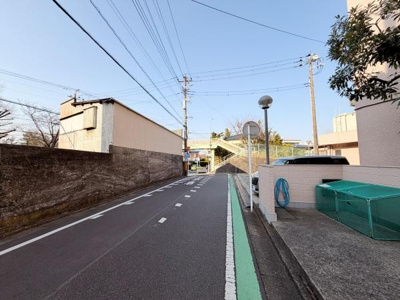 道路幅が広めで車両の通行や駐車もスムーズです。周囲には住宅や施設が点在し落ち着いた街並みが感じられます。道路脇には緑色ラインが施されており歩行者の安全にも配慮された設計です。