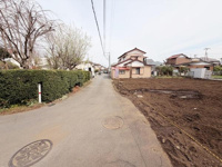 現地写真で前面道路の様子がよく分かります。周囲には家や植栽があり落ち着いた環境となっています。道路幅も確認しやすい写真です。前面道路の舗装状態も一目でわかります。