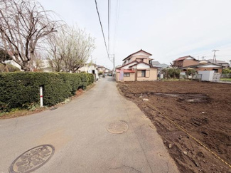 現地写真で前面道路の様子がよく分かります。周囲には家や植栽があり落ち着いた環境となっています。道路幅も確認しやすい写真です。前面道路の舗装状態も一目でわかります。
