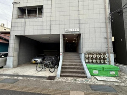 建物外観はシンプルなデザインで落ち着いた雰囲気が感じられます。入口前には駐輪スペースと駐車スペースが設けられており生活利便性が高い構造です。複数のガスメーターが整然と配置されているのも特徴的です。