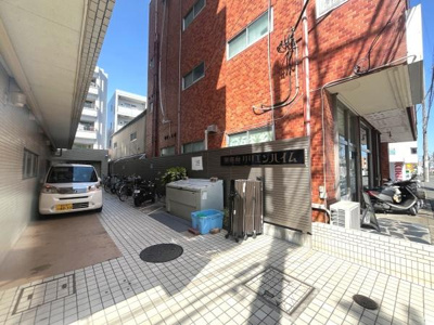 陽当たりのよいエントランスアプローチが印象的です。バイクや自転車も駐輪できるスペースが広く確保されています。車の駐車スペースも敷地内にございます。周囲には店舗も見られ利便性を感じさせる外観です。