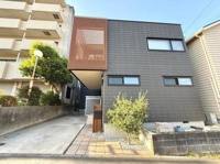 シンプルで洗練された外観が特徴の建物です。直線的なデザインと木目のアクセントが目を引きます。モダンなブラックの外壁が印象的です。広い駐車スペースも確保されています。植栽がアクセントになっています。