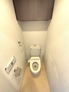 ウォシュレット機能付きのトイレ。ペーパーホルダーやタオル掛けは標準装備しています。上部には吊戸棚があるので、トイレットペーパーのストックや清掃道具等を収納するのに便利です。