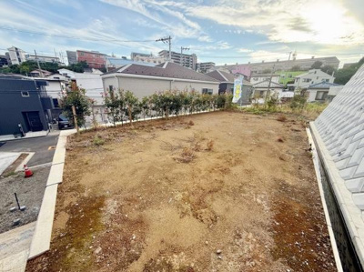 開放的な空間が広がる敷地の様子です。周辺には建物が立ち並び都市的な雰囲気を感じられます。段差のあるアプローチも敷地にアクセントを与えています。整備された道路に面している点も安心です。