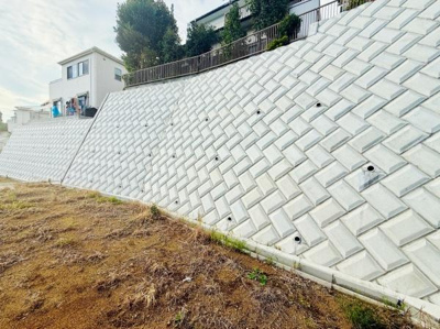 しっかりと整備された法面が安心感を与えます。コンクリートの施工が丁寧で見た目も清潔感があります。家屋が高台に位置しているため周囲も見渡しやすいです。斜面の安定感が印象的な一枚です。