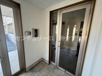 エントランスの明るいガラスドアが開放的な印象を与えます。防犯面も安心できるインターホンが設置されています。公共エリアの床タイルがすっきりとしたデザインを演出します。