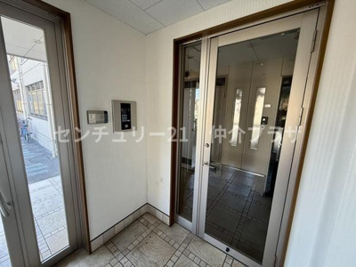 エントランスの明るいガラスドアが開放的な印象を与えます。防犯面も安心できるインターホンが設置されています。公共エリアの床タイルがすっきりとしたデザインを演出します。