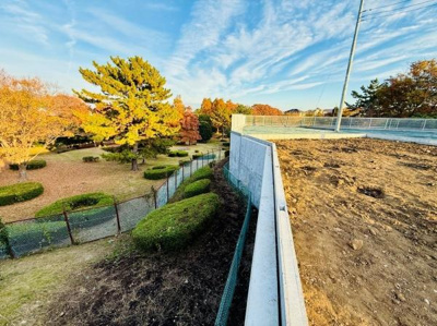 開放感のある現地土地写真です。周囲には緑も多く広々とした印象を受けます。敷地内の傾斜やフェンスが特徴的で視界が抜ける眺望が魅力的です。静かな環境でゆとりを感じられます。