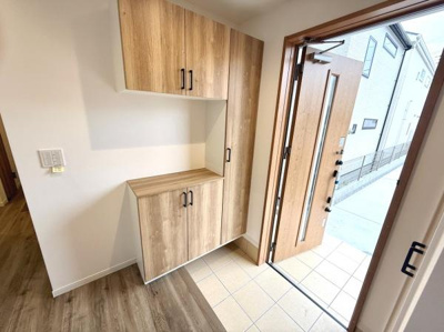 玄関には木目調の収納スペースが備わっておりすっきりとした空間を演出します。明るいタイル床が印象的でナチュラルな雰囲気が際立ちます。玄関扉は採光窓付きで自然光が入りやすい設計です。