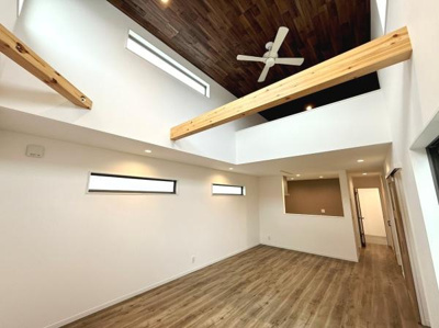 吹き抜け天井が開放感を演出しています。木目調のフローリングと天井が温かみを感じさせます。スリット窓からやわらかい自然光が差し込みます。梁のアクセントが個性的な雰囲気をプラスしています。