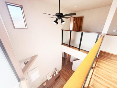 吹き抜けの空間が開放感を演出しており自然光もたっぷりと差し込みます。シーリングファンが設置されており空気の流れも快適です。木目調のフローリングと階段が温かみを感じさせます。