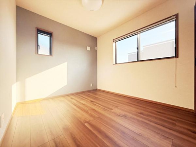 明るい光が差し込む洋室で落ち着いた色合いの壁が印象的です。木目調のフローリングが空間をすっきり見せています。二つの窓から自然光がしっかり入ります。快適に過ごせる環境が整っています。