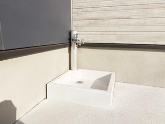 屋外に設置されたシンプルな水栓付き流しです。角に設けられており作業時にも使いやすい形状です。白を基調としたデザインが外観と調和しています。掃除や手洗いなど多用途に利用可能です。