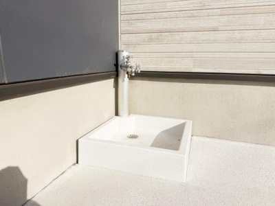 屋外に設置されたシンプルな水栓付き流しです。角に設けられており作業時にも使いやすい形状です。白を基調としたデザインが外観と調和しています。掃除や手洗いなど多用途に利用可能です。