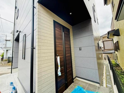 直線的なデザインが印象的な玄関です。木目調の扉が外壁と調和し落ち着いた雰囲気を演出しています。玄関周りのスペースも確保されていてスムーズに出入りができます。シンプルながら現代的な外観です。