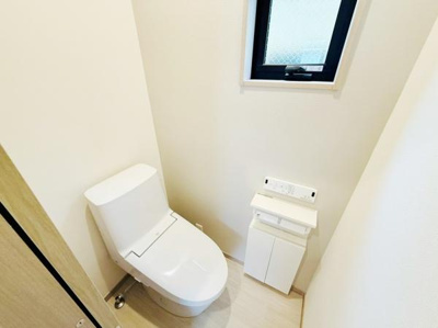 明るい室内に設置されたトイレです。小窓から自然光が入るので圧迫感の少ない空間です。操作パネルや収納も備わっています。シンプルで清潔感があります。