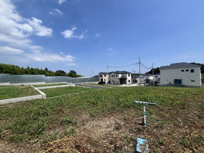 広い空の下ゆとりある空間が広がる現地土地写真です。周囲に新しい住宅が並び開放的な印象を与えます。整然とした区画で落ち着いた住環境を感じることができます。緑も多く周囲との調和が取れています。