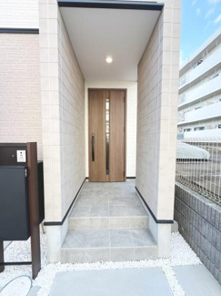 シンプルで落ち着いた印象の玄関です。タイル張りのアプローチは見た目にも清潔感があります。屋根付きのため雨の日も安心して利用できます。木目調のドアがアクセントになっています。