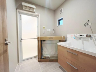 明るい色合いの床と壁で清潔感のある印象です。大きな洗面ボウルは使い勝手がよさそうです。小窓があり換気にも配慮されています。エアコンも設置されています。全体的に効率的な配置が特徴です。