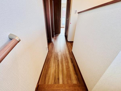 ナチュラルな色合いのフローリングが特徴の廊下です。手すりも設置されており安全面に配慮されています。明るい照明が空間をすっきりと見せています。壁面のクロスもシンプルで落ち着いた印象です。